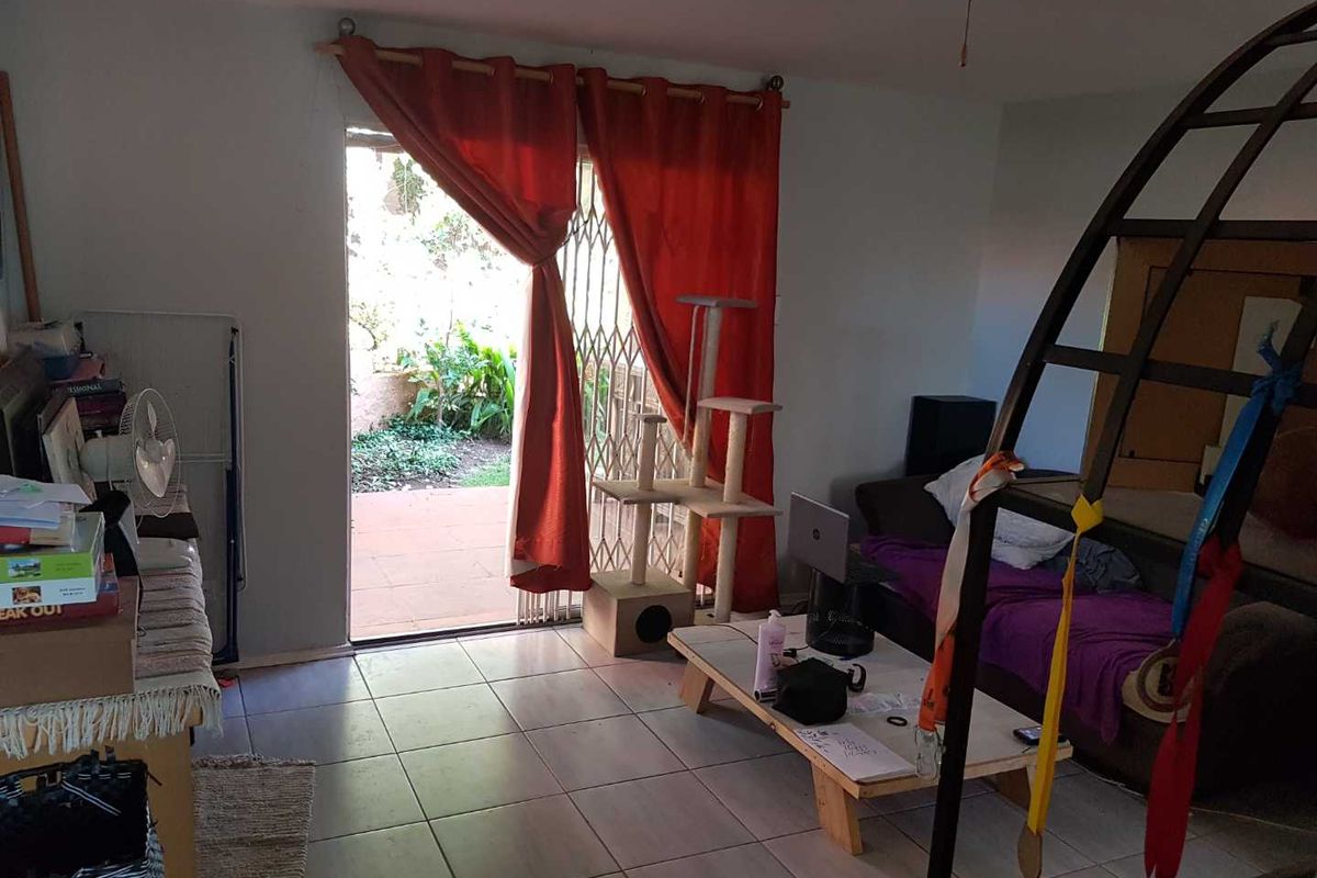 A living room area featuring tiled flooring and a sliding glass door with security gate leading to an outdoor patio space.