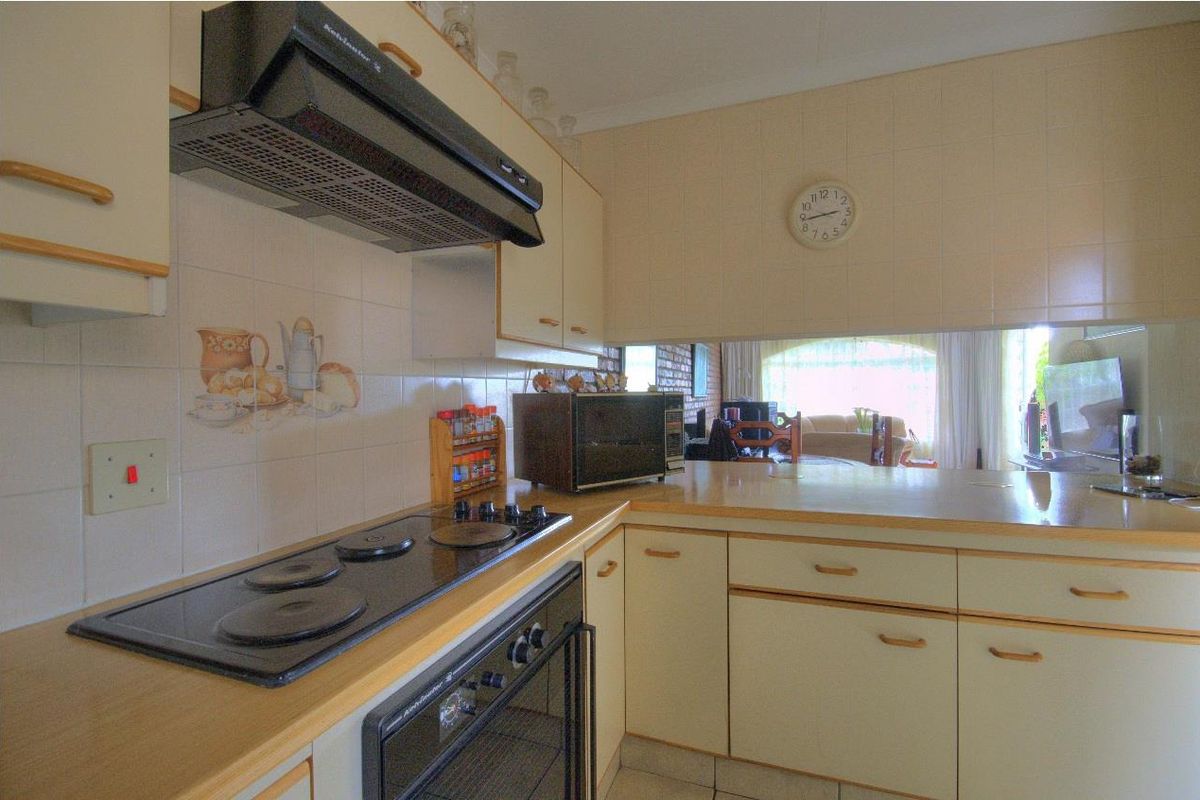 A functional kitchen featuring built-in cabinetry, an electric hob, oven, and extractor fan, with a pass-through window overlooking the adjacent living area.