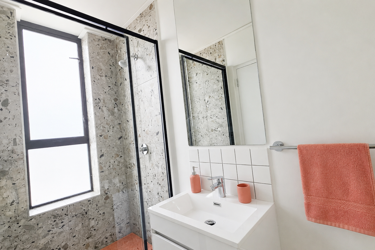 Modern bathroom featuring a walk-in shower with black-framed glass, terrazzo-style tiling, and a sleek vanity basin with a wall-mounted mirror.