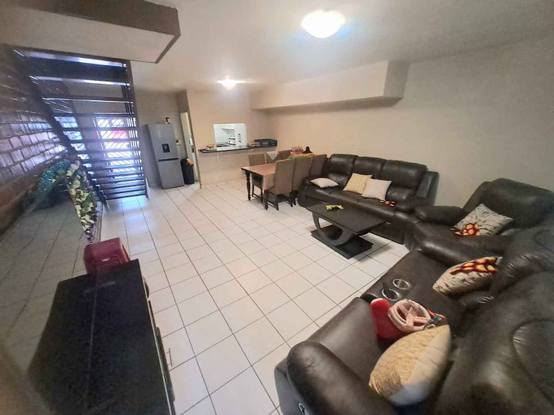 Open-plan living and dining area featuring ceramic floor tiles, a staircase, and a convenient pass-through window connecting to the kitchen space.