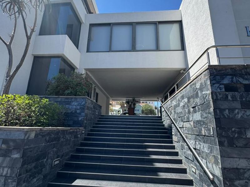 Modern office building entrance featuring a prominent stone-clad staircase, stainless steel handrails, and a covered walkway leading to the main building access.