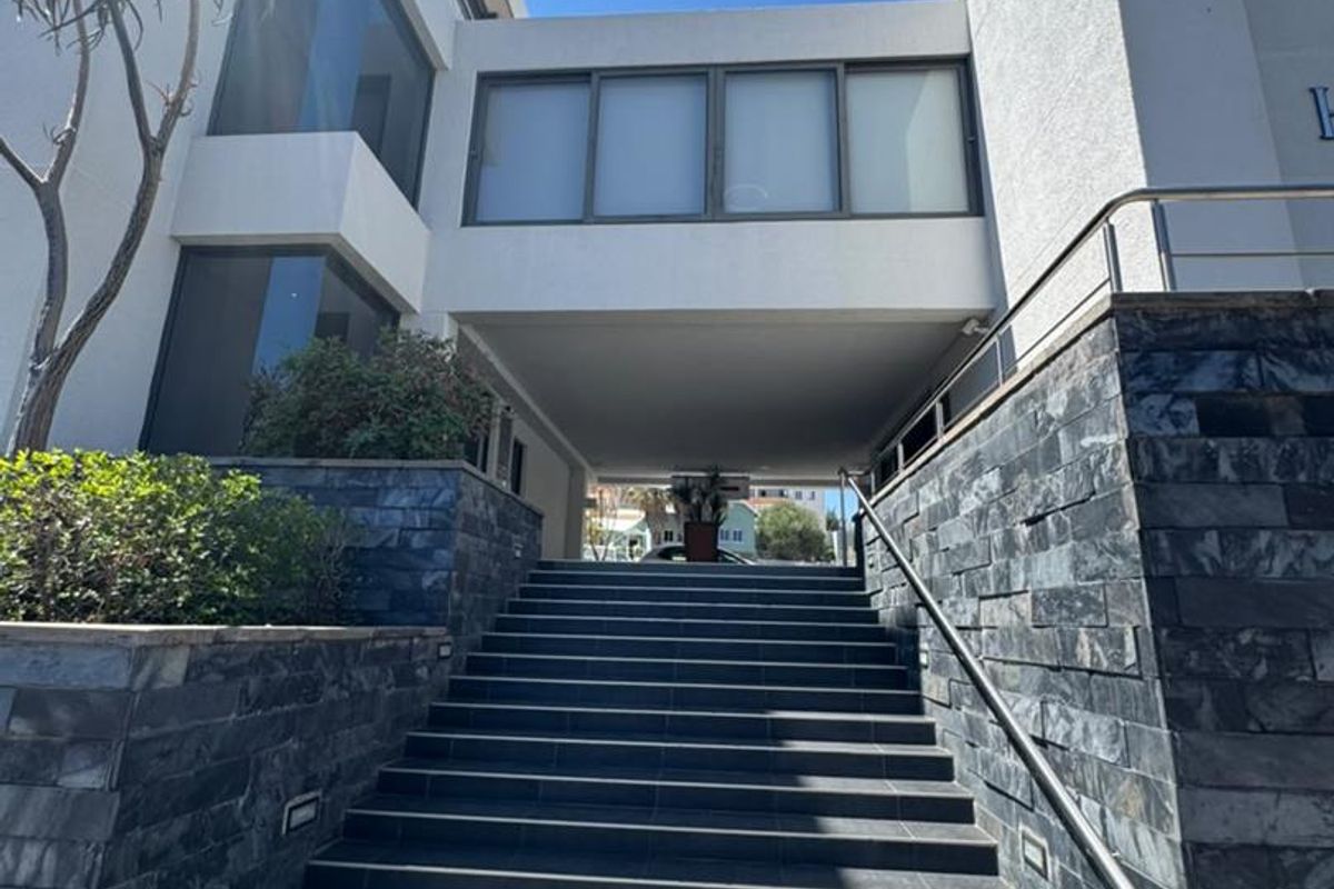 Modern office building entrance featuring a prominent stone-clad staircase, stainless steel handrails, and a covered walkway leading to the main building access.