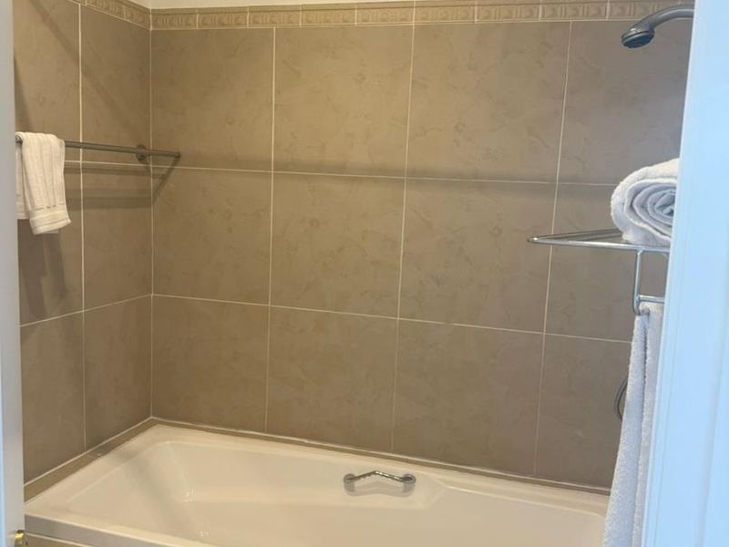 A functional bathroom featuring a built-in bathtub with shower head, neutral wall tiling, and an integrated extractor fan.