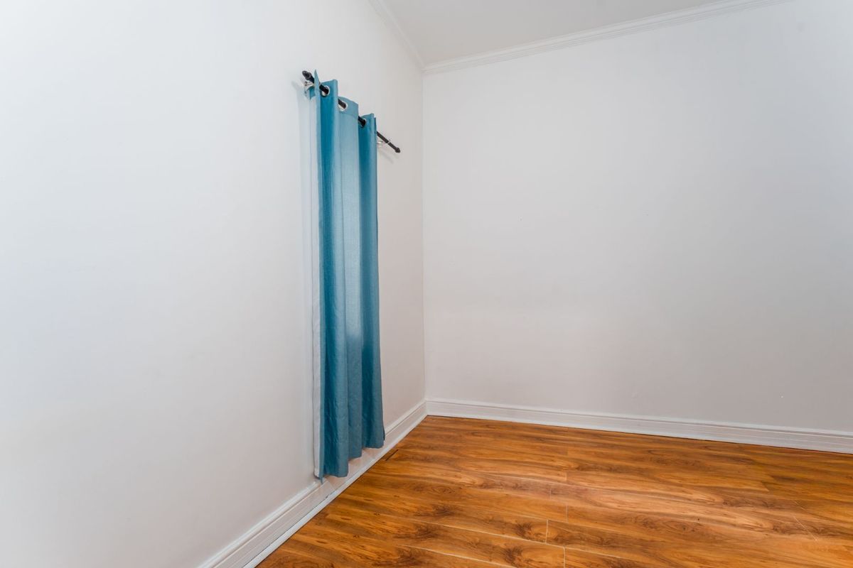 A bright, empty room featuring wood-look laminate flooring, white walls, and crown molding, providing a clean and versatile space.