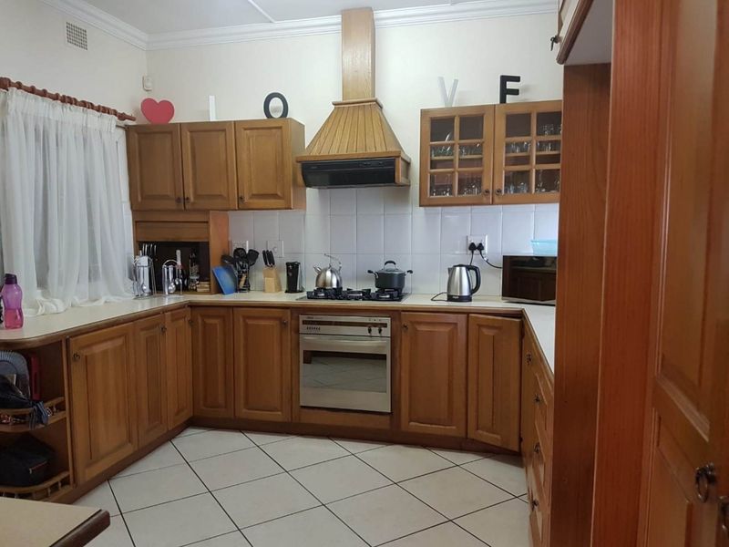 A functional kitchen featuring traditional wooden cabinetry, a built-in oven with gas hob, extractor fan, and tiled flooring with a neutral backsplash.