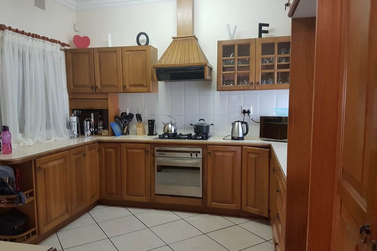 A functional kitchen featuring traditional wooden cabinetry, a built-in oven with gas hob, extractor fan, and tiled flooring with a neutral backsplash.