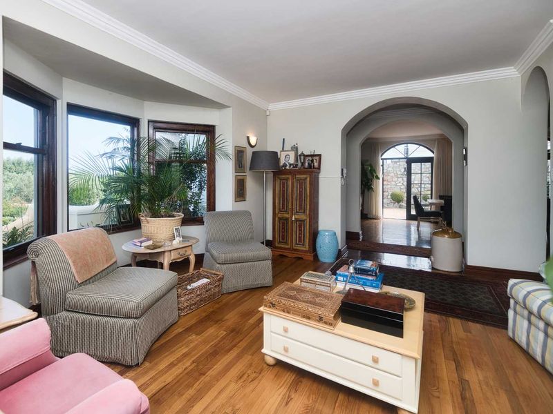 A cozy living room featuring polished hardwood floors, crown molding, and a bay window, with an arched transition leading to an adjacent space.