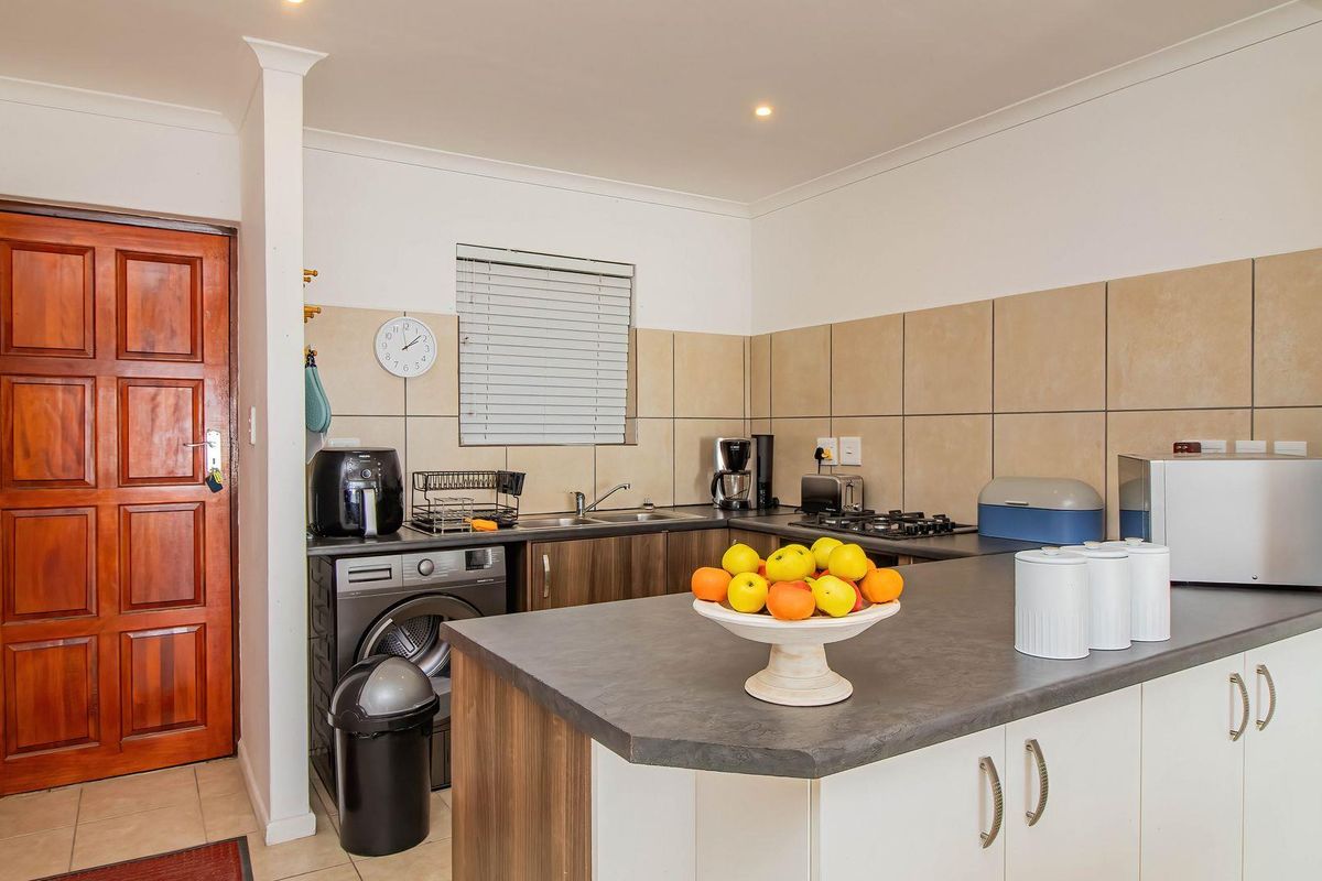 Functional kitchen featuring built-in cabinetry, laminate countertops, a gas hob, and tiled backsplash, with an integrated laundry area and direct access to the entrance.