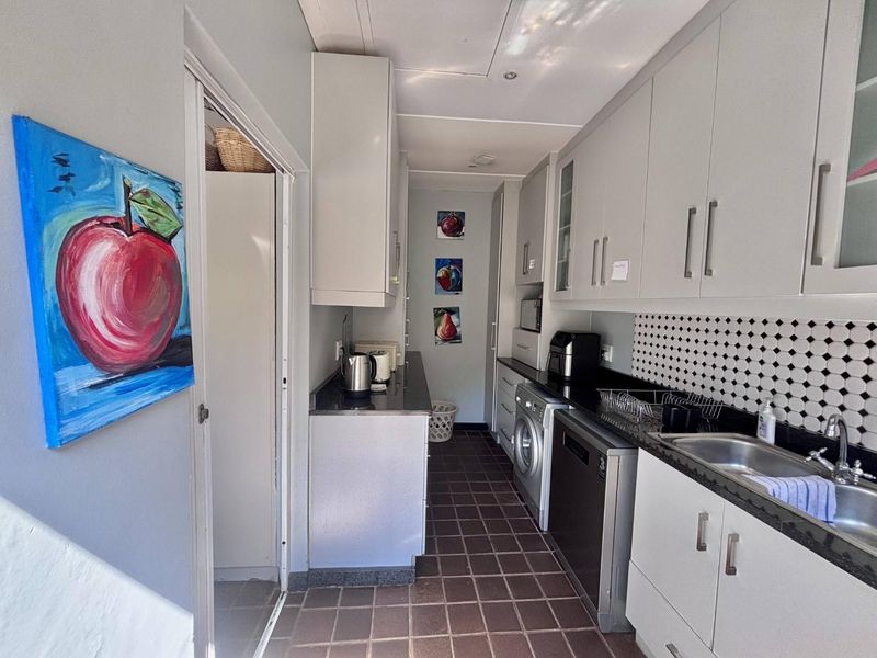 A functional scullery featuring built-in cabinetry, granite countertops, a stainless steel sink, and a mosaic tile backsplash with tiled flooring.