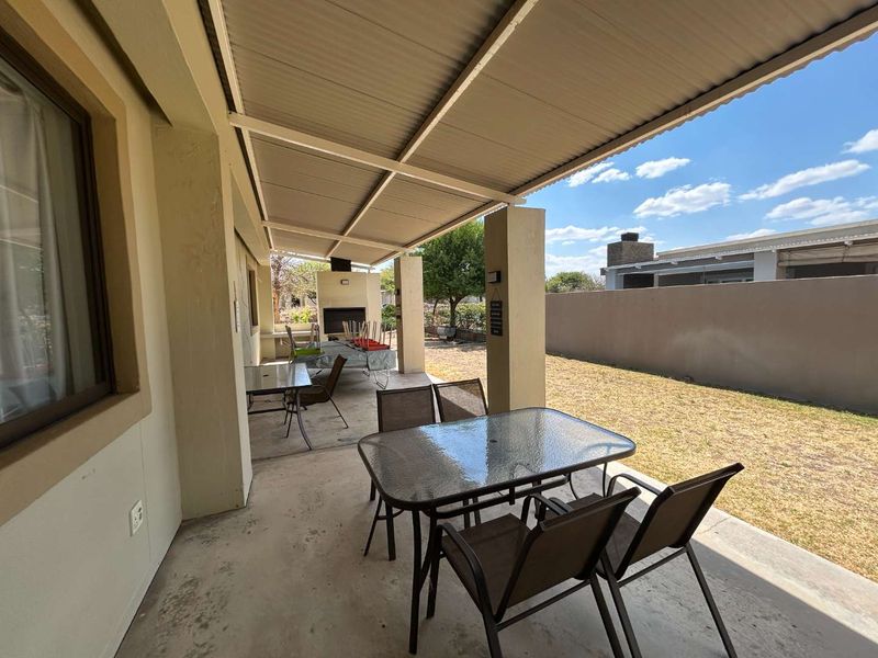 A covered outdoor patio area featuring a built-in braai and concrete flooring, overlooking a private rear garden with perimeter walling.
