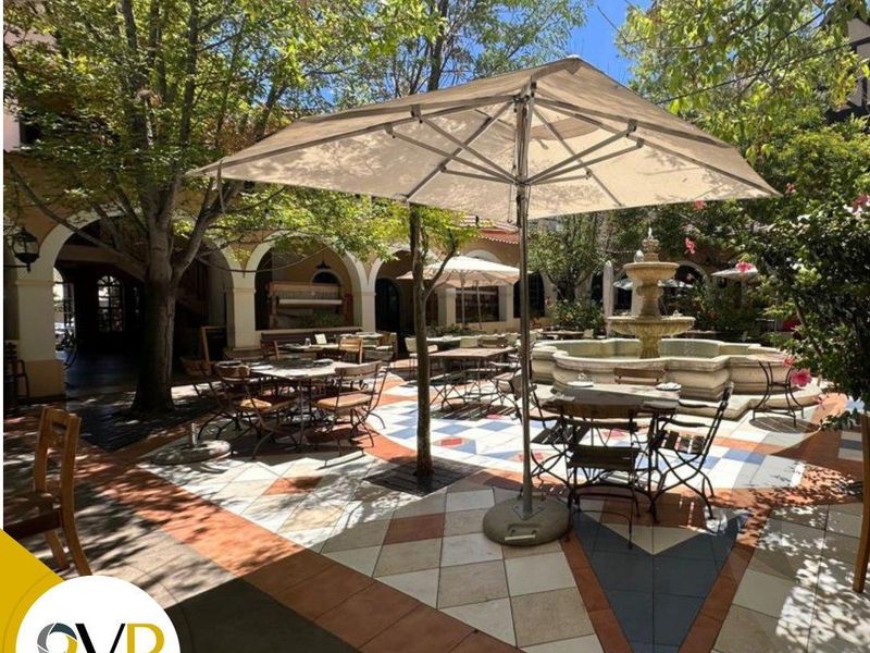 A charming outdoor courtyard featuring a central stone fountain, decorative patterned tile flooring, and an arched colonnade providing a pleasant shaded seating area.