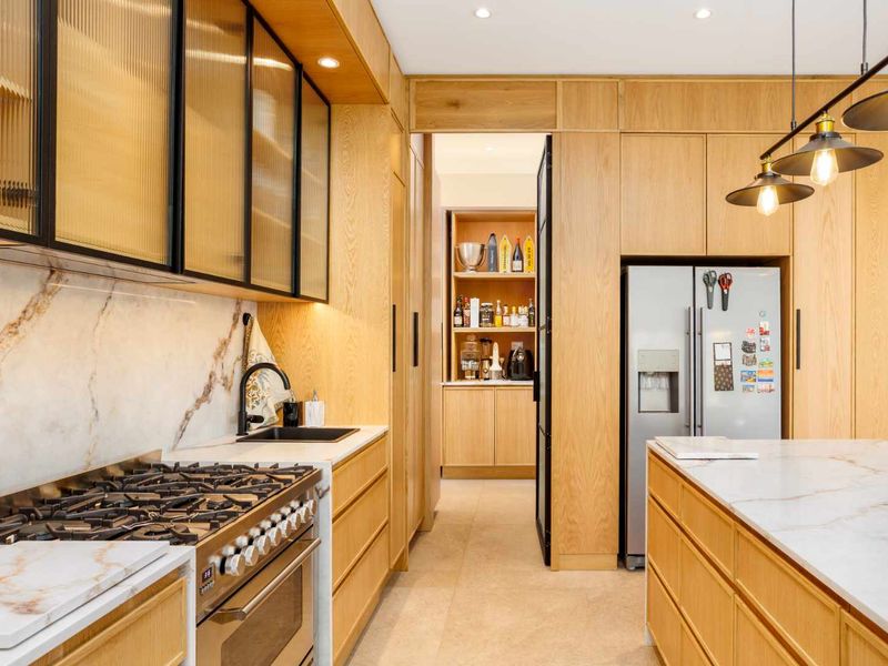 Modern kitchen featuring custom oak cabinetry, marble-look stone countertops, high-end gas range, and an adjoining scullery with integrated storage.