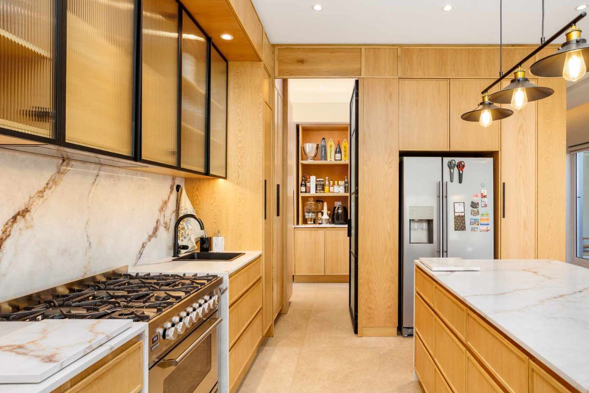Modern kitchen featuring custom oak cabinetry, marble-look stone countertops, high-end gas range, and an adjoining scullery with integrated storage.