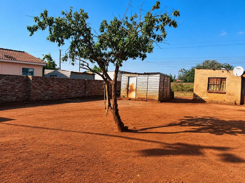 A spacious rear yard featuring a large dirt area, a brick boundary wall, and a metal storage shed.