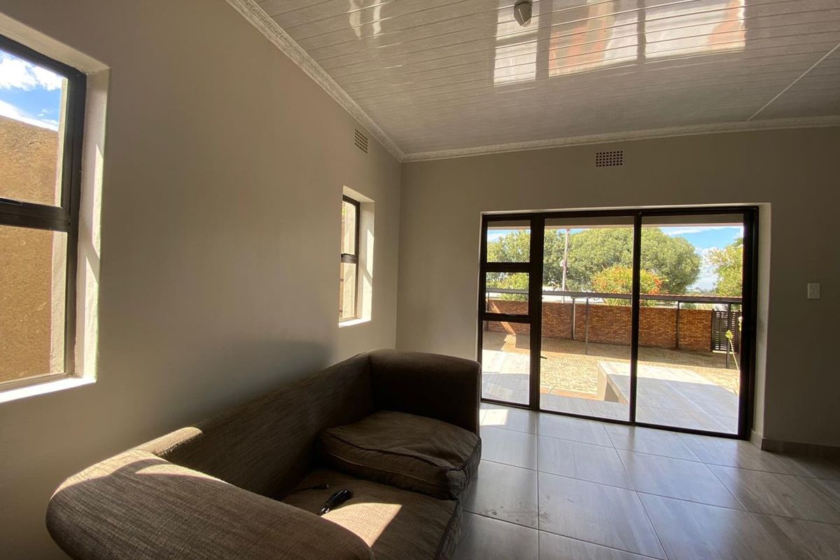 A bright living area featuring tiled flooring, crown molding, and large sliding glass doors that open onto an outdoor patio space.