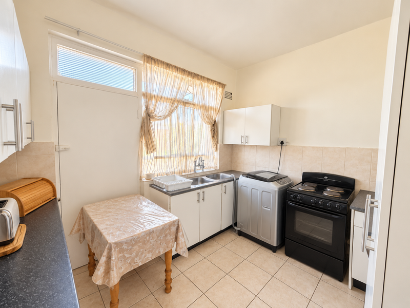 Functional kitchen featuring tiled flooring, built-in cabinetry, a double sink, and a freestanding stove with an extractor fan.