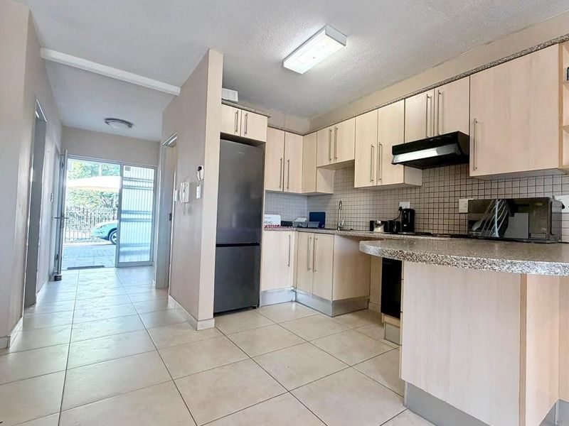A functional kitchen featuring light wood cabinetry, granite countertops, tiled backsplash, and a breakfast nook, with direct access to the entrance hallway.