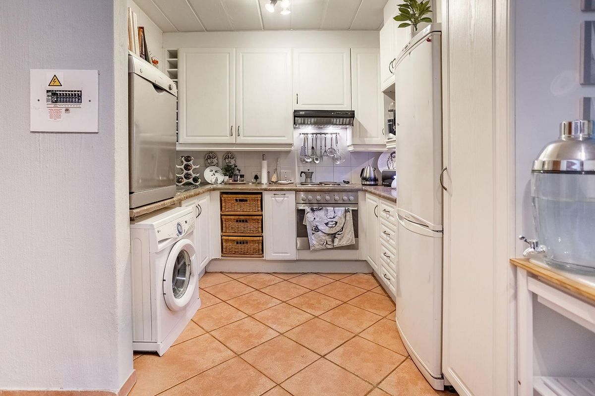 Compact kitchen featuring white cabinetry, tiled flooring, built-in oven, extractor fan, and integrated laundry appliance space.