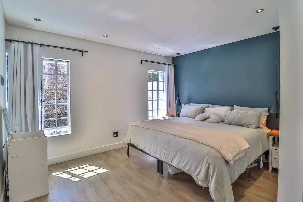 A well-lit bedroom featuring light wood-look flooring, recessed ceiling lighting, and a prominent blue accent wall.