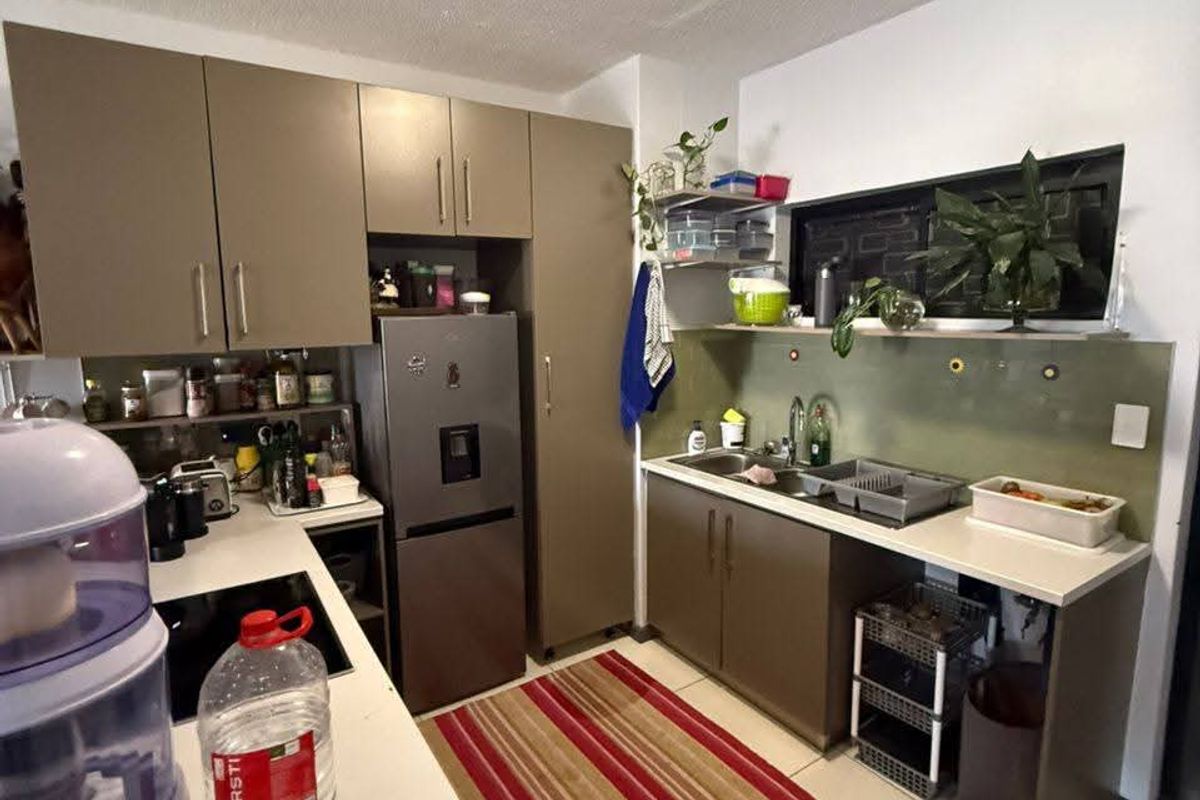 A functional kitchen featuring taupe cabinetry, a stone-look countertop, a stainless steel sink, and a glass splashback.