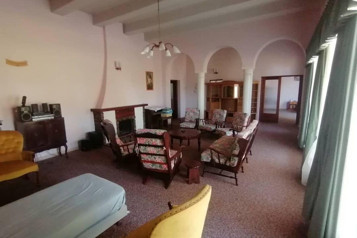 Spacious living room featuring exposed ceiling beams, a brick fireplace, and arched architectural details leading to an adjacent area.