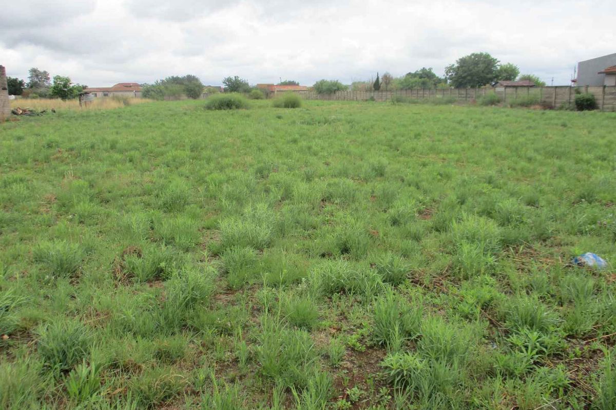 A vacant residential plot featuring open grass land enclosed by perimeter walls and fencing.