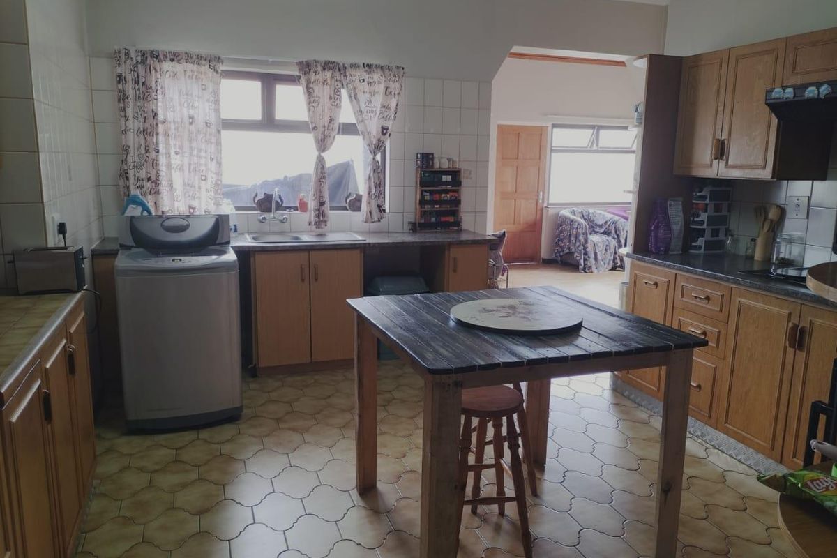 A functional kitchen featuring wooden cabinetry, tiled splashbacks, and a central workspace, with an adjacent room visible through the doorway.