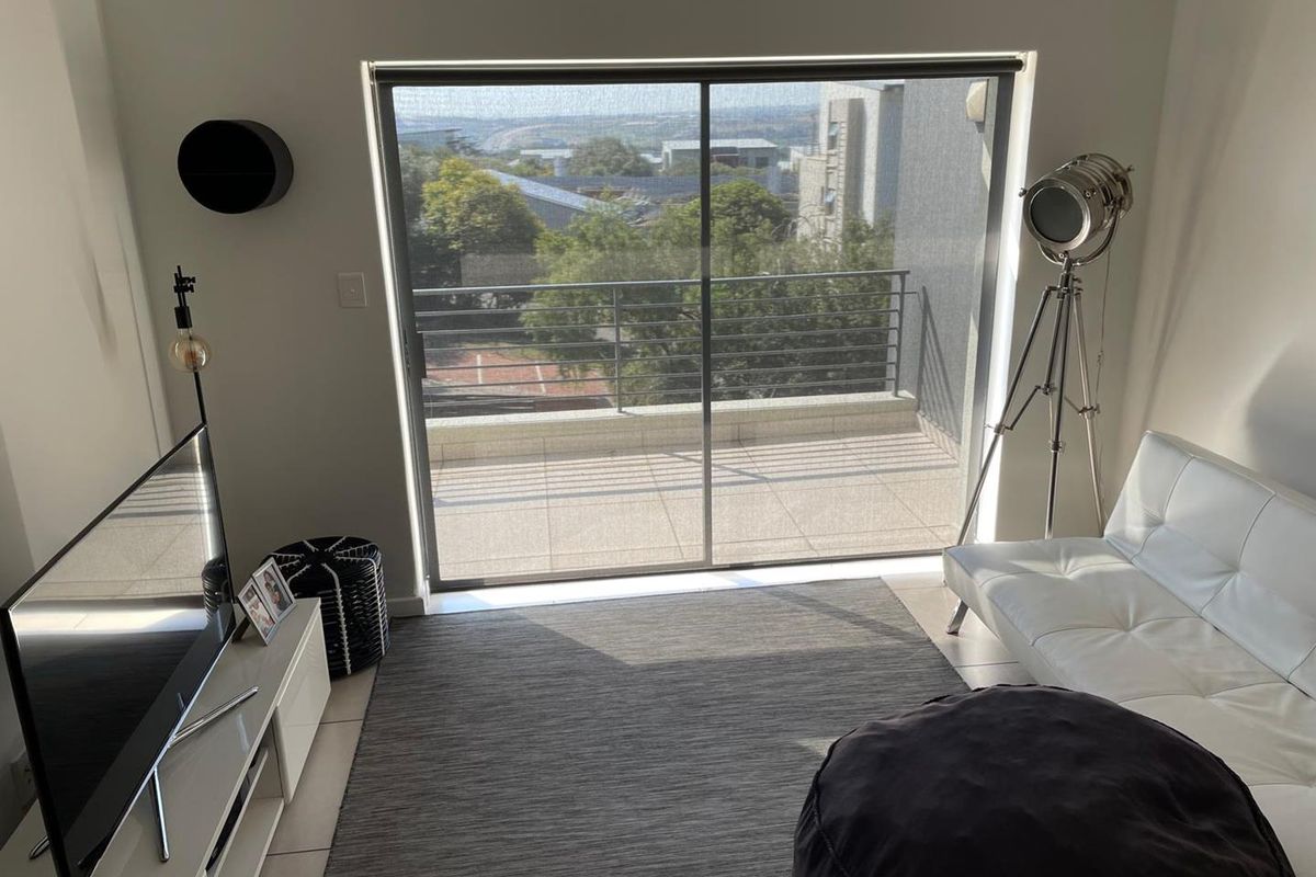 A bright living room featuring large sliding glass doors that open onto a private balcony with an elevated neighborhood view.
