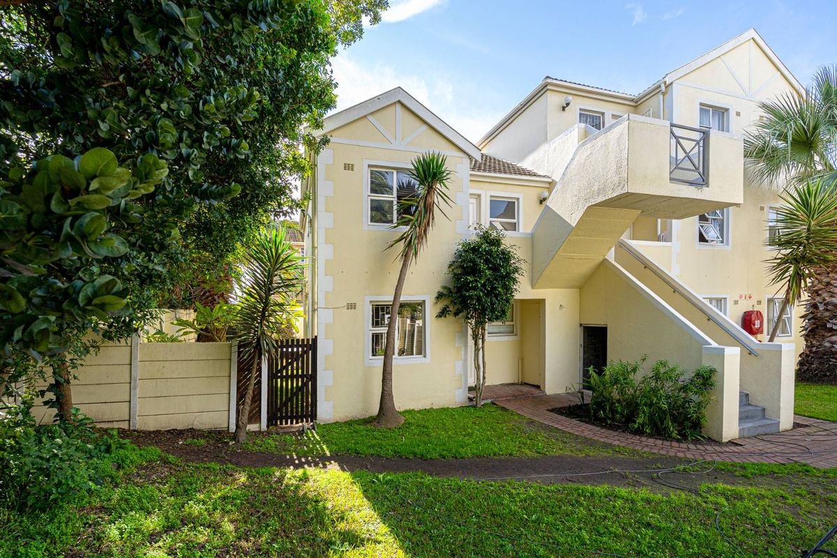 Rear view of the apartment complex featuring a paved walkway, external staircase, and established garden area with boundary walling.