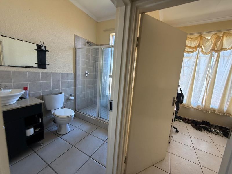 A functional bathroom featuring a shower enclosure, vanity cabinet with basin, and toilet, with tiled flooring and wall finishes.