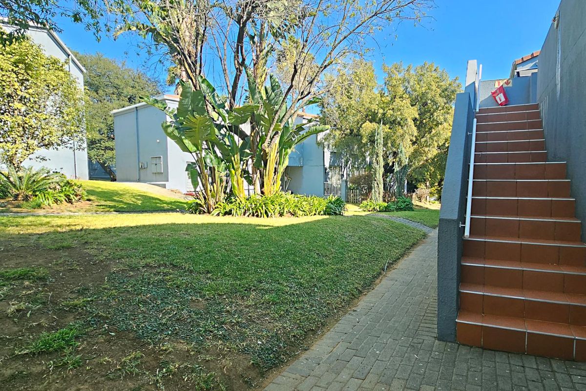 Exterior view of the apartment complex featuring a paved walkway, tiled outdoor staircase, and landscaped garden area with mature trees.