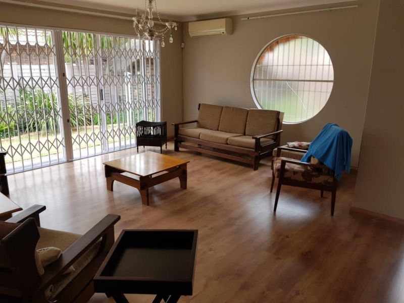 Spacious living room featuring laminate flooring, a split-system air conditioner, and a unique circular window, with direct access to the outdoor area via sliding doors.
