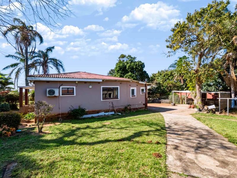Rear view of the house featuring a concrete driveway, established garden, and exterior wall with an installed air conditioning unit.