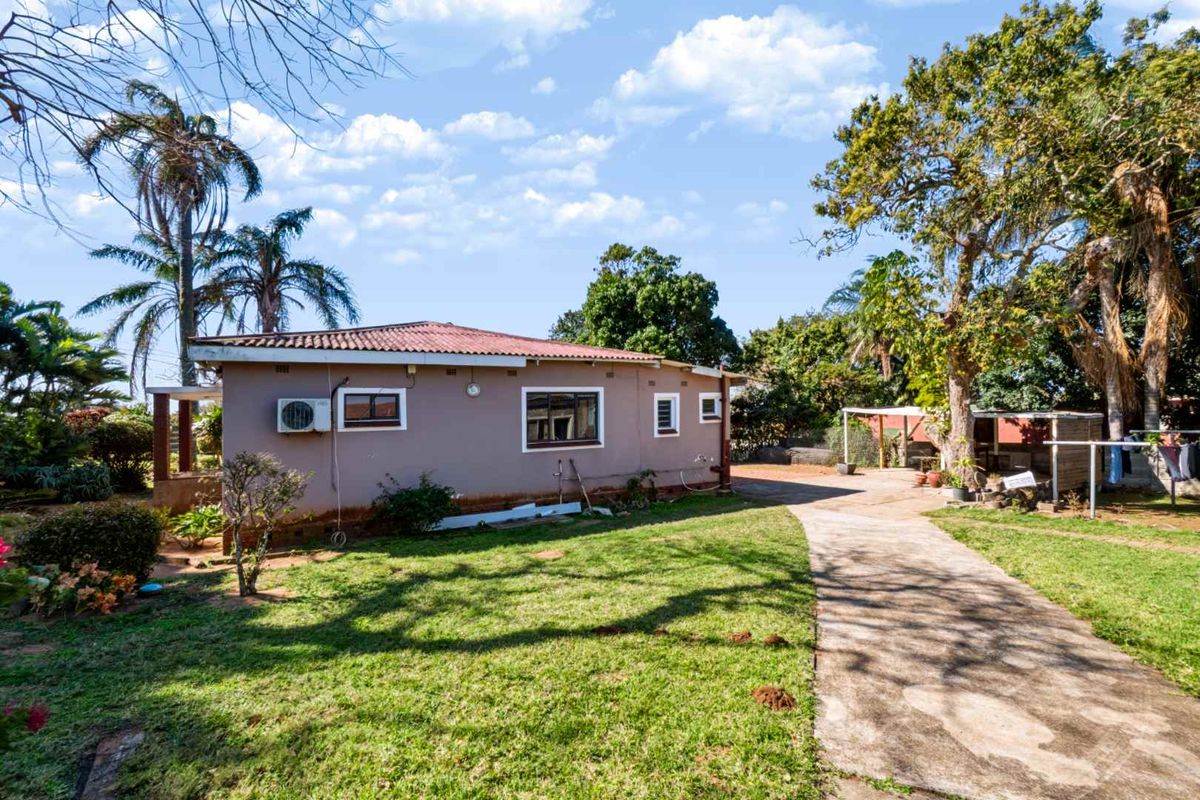 Rear view of the house featuring a concrete driveway, established garden, and exterior wall with an installed air conditioning unit.