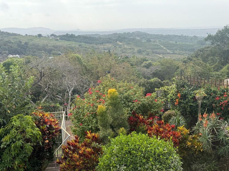 A scenic elevated view overlooking a lush, landscaped garden with a metal staircase leading down, set against a backdrop of rolling hills and greenery.