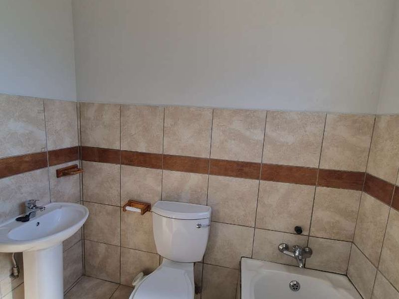 A functional bathroom featuring a pedestal basin, standard toilet, and bathtub with neutral wall and floor tiling.