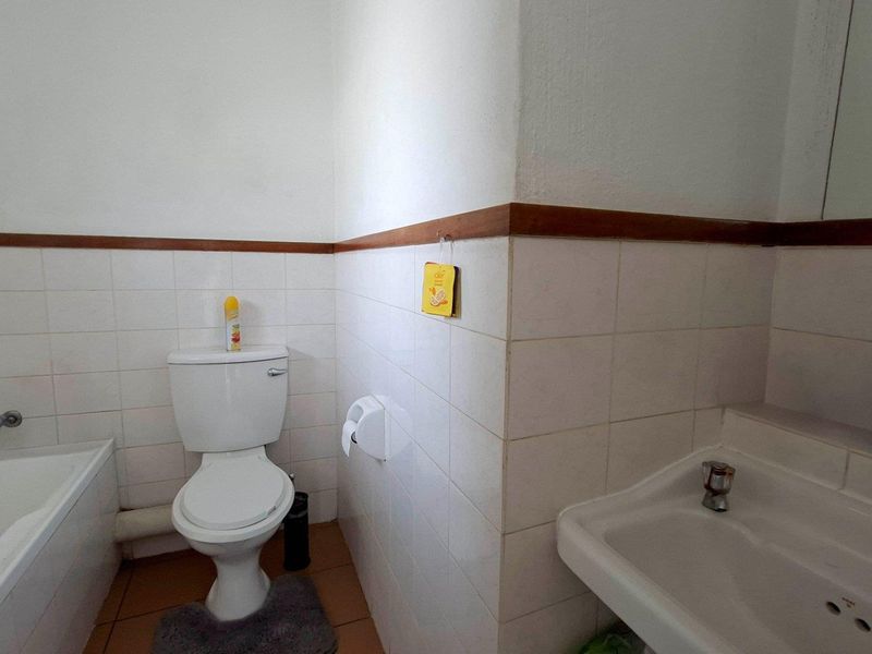 A functional bathroom featuring a bathtub, toilet, and washbasin with classic white wall tiling and a wooden dado rail.