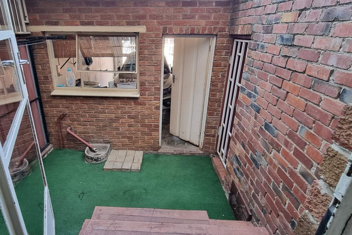 A small, enclosed rear courtyard area featuring exposed brick walls, a security gate, and direct access to the property interior.