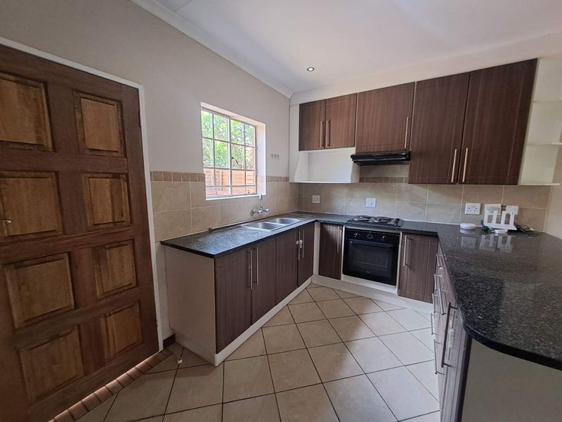 A functional kitchen featuring dark wood cabinetry, granite countertops, a built-in oven with gas hob, and tiled flooring with a neutral backsplash.