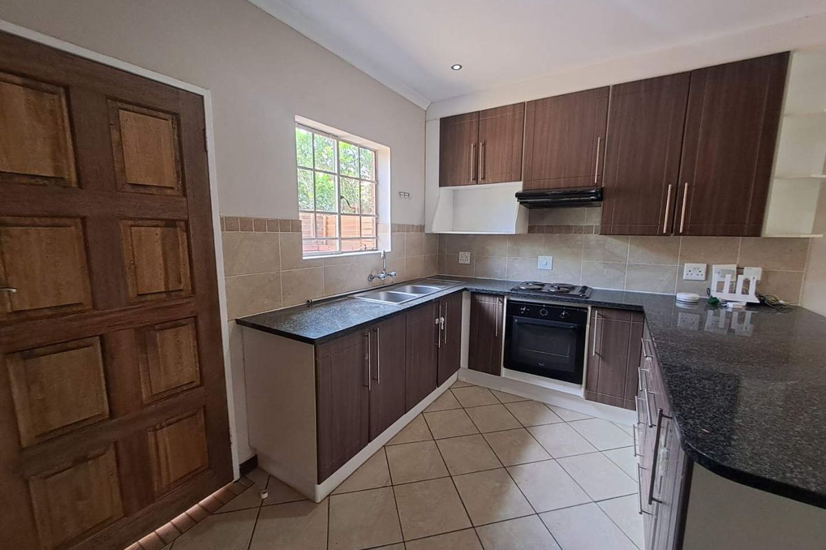 A functional kitchen featuring dark wood cabinetry, granite countertops, a built-in oven with gas hob, and tiled flooring with a neutral backsplash.