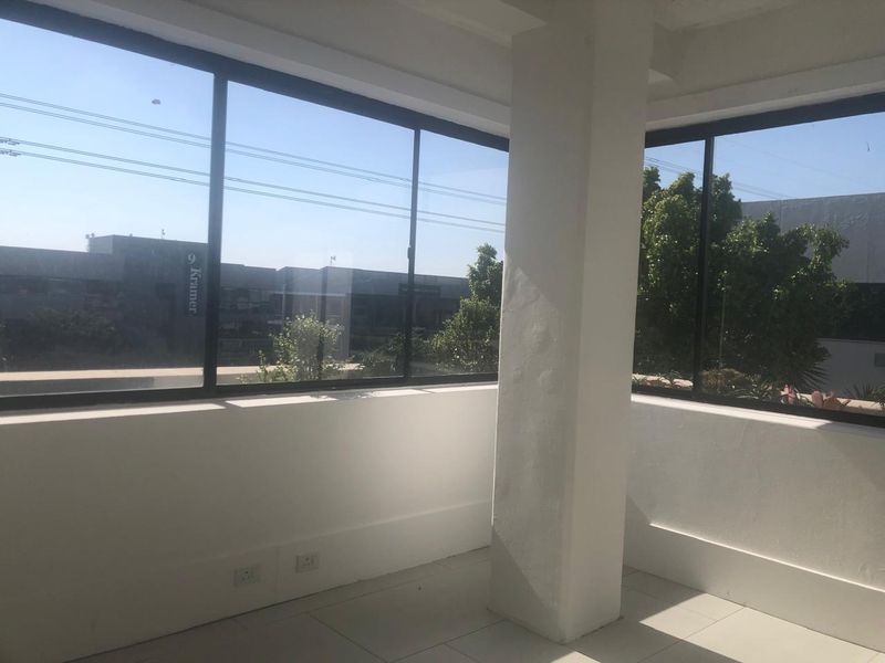 A bright, empty office space featuring large windows with natural light, tiled flooring, and a central structural column.