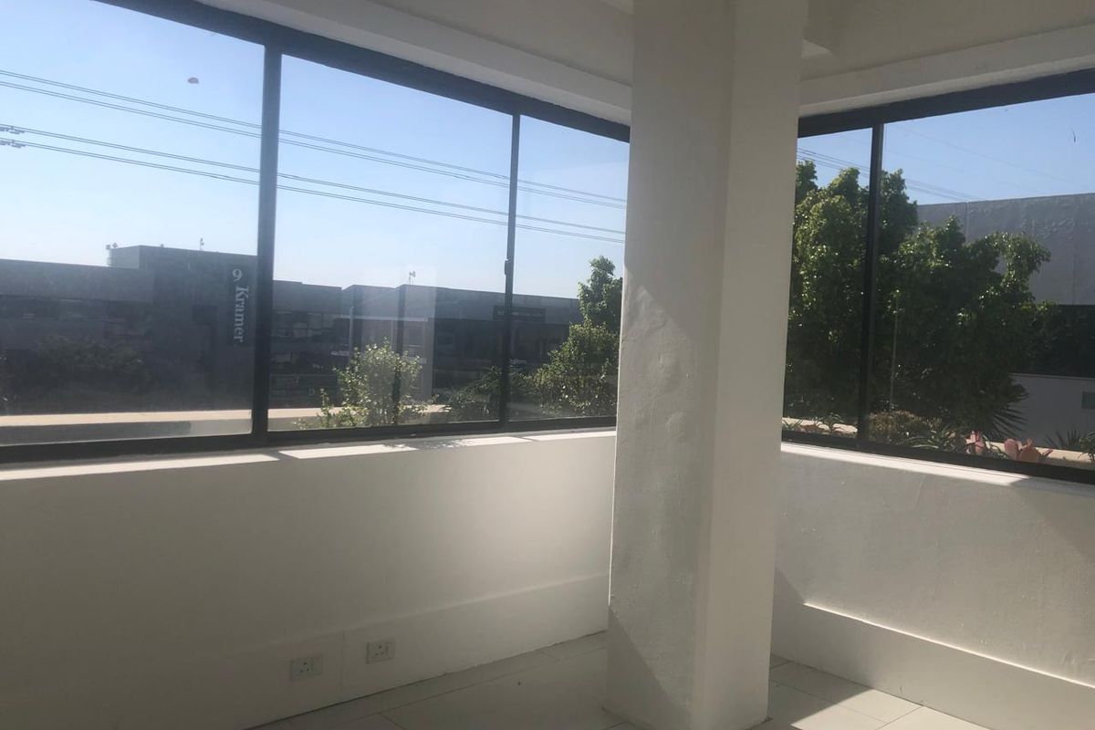 A bright, empty office space featuring large windows with natural light, tiled flooring, and a central structural column.