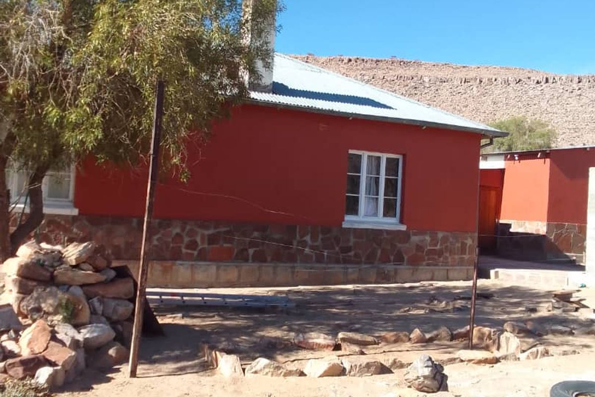 Exterior view of a farm dwelling featuring a red facade with stone cladding base, corrugated metal roof, and a prominent chimney.