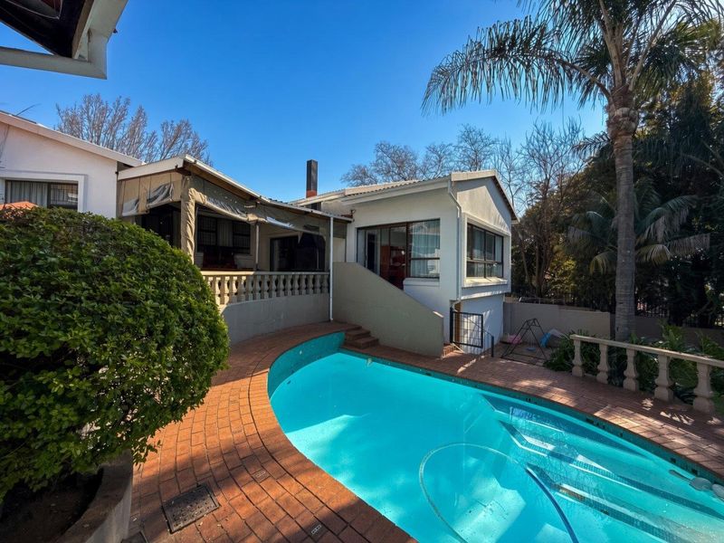 Outdoor pool area featuring brick paving, a covered patio with balustrades, and a well-maintained swimming pool set against the rear building elevation.