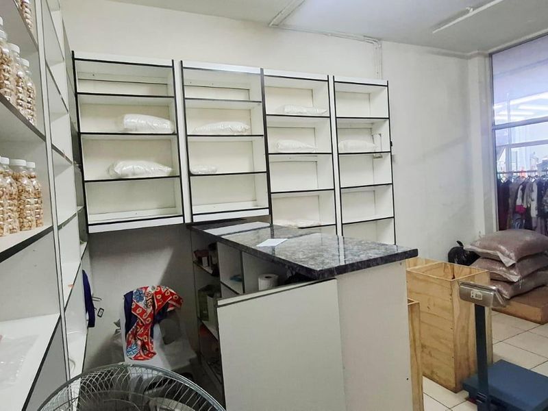 A functional retail or utility space featuring built-in shelving units, a service counter, and tiled flooring with direct street-facing glass access.