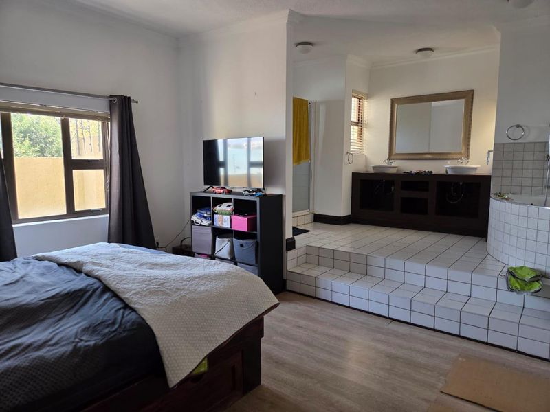 Spacious bedroom featuring an open-plan en-suite bathroom on a raised tiled platform with a dual vanity and built-in bathtub.