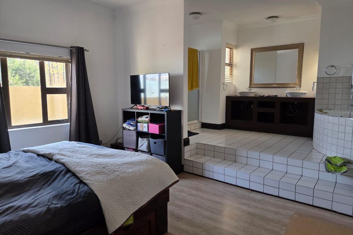 Spacious bedroom featuring an open-plan en-suite bathroom on a raised tiled platform with a dual vanity and built-in bathtub.