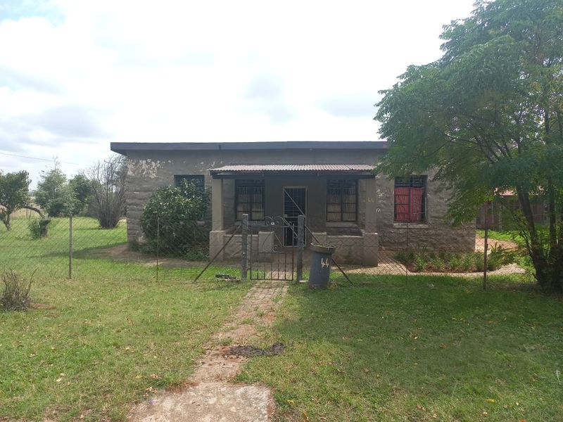 Front view of a single-story detached house featuring a covered porch, metal security gate, and a large surrounding garden area.