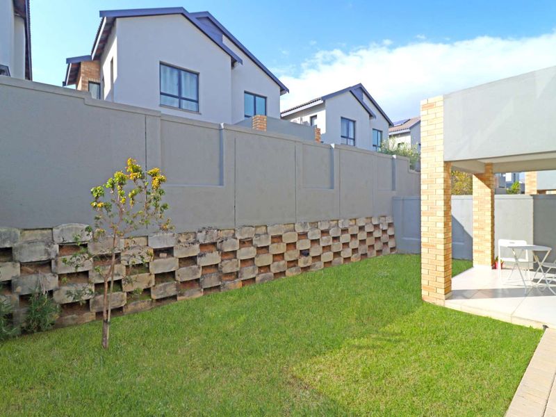 A private rear garden featuring a lawn, a covered patio with brick pillars, and a decorative concrete block retaining wall.