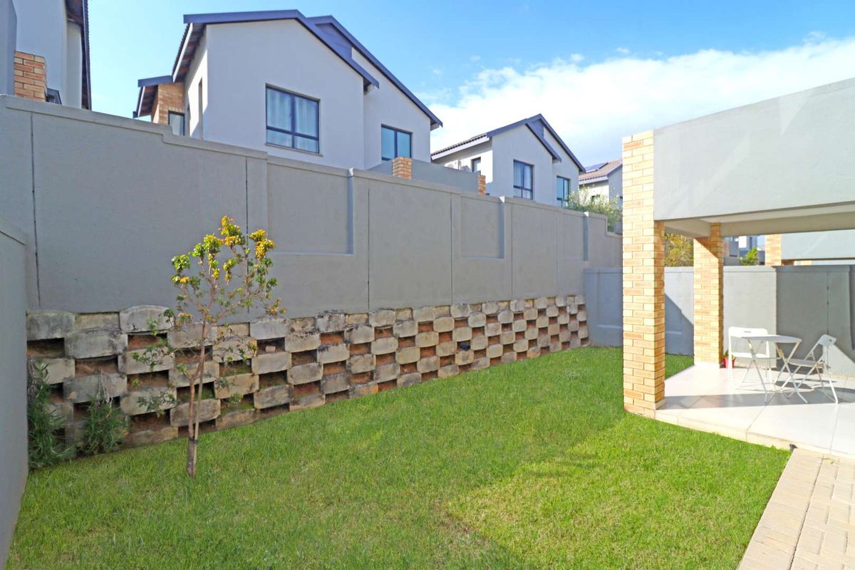 A private rear garden featuring a lawn, a covered patio with brick pillars, and a decorative concrete block retaining wall.